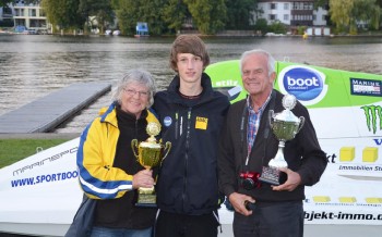 Max Stilz mit den Besuchern, Pokalen und dem Motorboot dahinter.